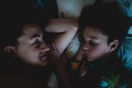 Mom looks at the sleeping child. Morning waking up. The little boy is sleeping near my mother. Sleepy baby. Mother's love. Night sleep.の写真素材