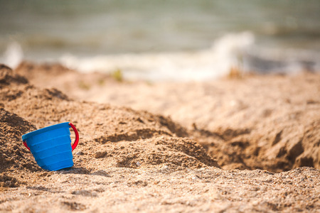A plastic pail in the sand. Baby bucket seashore. Working tool against the background of the sea coast. Children's plastic bucket.の写真素材