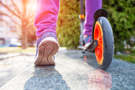 Feet on the scooter. The girl in the jeans riding a scooter around the city. Active rest in the fresh air. The scooter wheel closeup.の写真素材