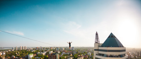 A man walks along a line stretched between two buildings. A man catches balance at altitude....