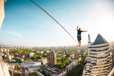 A man walks along a line stretched between two buildings. Extreme entertainment. Fear of heights. The man is balancing over the city.の写真素材