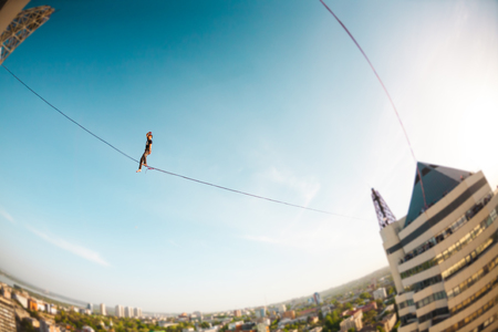 A man walks along a line stretched between two buildings. A man catches balance at altitude. Highline over the city.の写真素材