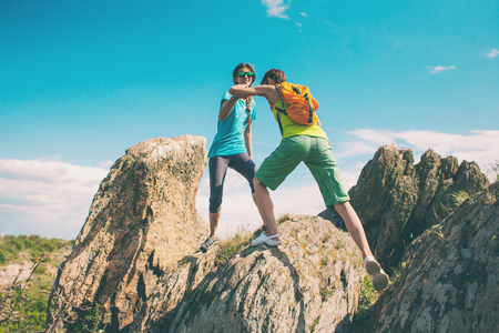 A woman travels. The girl is walking along the stony road. Tourist with a backpack in the background of the mountains. Two friends travel together. The girl holds out her hand to friend. Helping hand.の写真素材