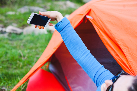 The girl is taking pictures near the tent. A woman is resting in nature. Camping in the forest. The brunette takes pictures of nature on the phone.の写真素材