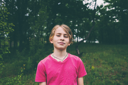 Portrait of a boy in the forest. Portrait of a child. Blond in the background of trees. A teenager with long hair.の写真素材