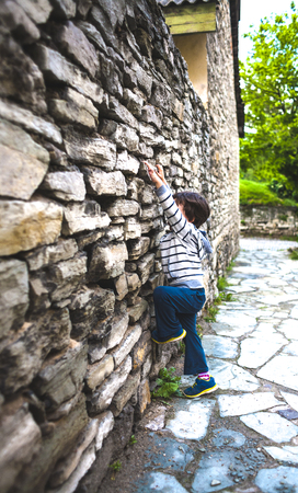 A restless child. Fidget. The boy climbs the ancient stone fence. The child is trying to climb a stone wall. An old brick wall. A little rock climber. Childish curiosity.の写真素材