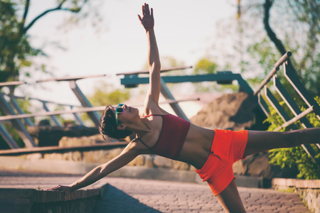 A woman is doing stretching in a city park. Morning training in nature. Yoga practice. Fitness. The girl warms up before jogging.の写真素材