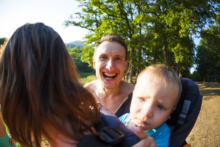 The family spends time together in nature. Loving father. A man looks at the child and smiles. The boy is sitting in a backpack. The woman has a son. Happy day. Emotional person.の写真素材
