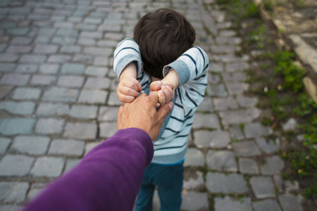 The boy is pulling his father's hand. Dad walks with his son along the city street. The child is capricious and does not let go of the parent's hand.の写真素材