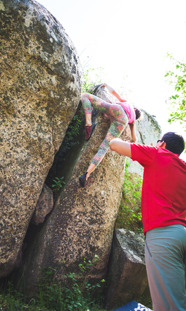 Climbing in nature. Friends climb to the stone. The girl climbs on the stone, and friends support her. Bouldering in nature. Active lifestyle. Sports people. Gymnastic insurance.の写真素材