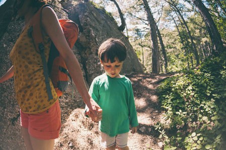 A woman and her child walk along a forest trail. A boy with a backpack travels with his mother. Hike with children. The kid walks through the pine forest. Active summer holidays. Fisheye lens.の写真素材
