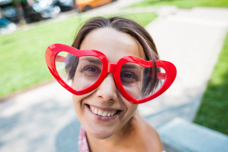 Girl with glasses in the shape of heart. Portrait of a woman in funny glasses. Smiling brunette...