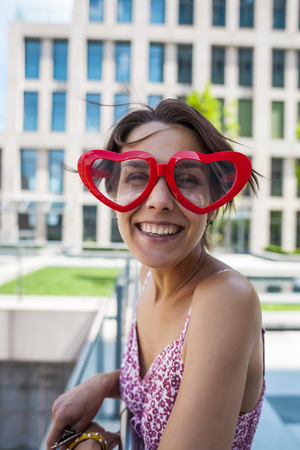 Girl with glasses in the shape of heart. Portrait of a woman in funny glasses. Smiling brunette having fun on the street.の写真素材