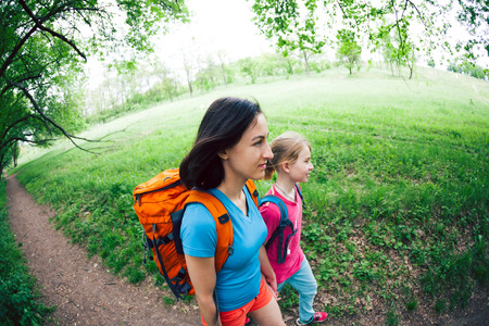 A woman with child goes hiking. The woman took her sons by the arms. Traveling with family. The boy walks with his mother in the forest. Hike with backpacks.の写真素材