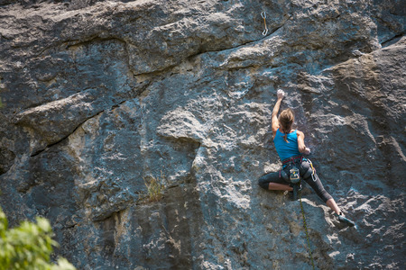 The girl climbs the rock. The climber is training to climb the rock. A strong athlete overcomes a difficult climbing route. Extreme hobby. A woman goes in for sports in nature. Natural rocky terrain.の写真素材