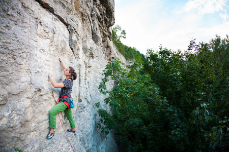 A woman trains in nature. Active lifestyle. The girl climbs the rock. Climber overcomes difficult...