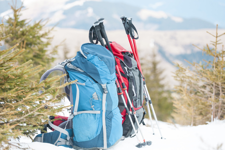 Two backpacks in the background of snow-capped mountains and blue sky. A backpack on the snow. Active lifestyle. Trekking in winter. Equipment for hiking. Trekking sticks.の写真素材
