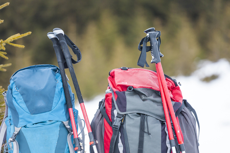 Two backpacks in the background of snow-capped mountains and blue sky. A backpack on the snow. Active lifestyle. Trekking in winter. Equipment for hiking. Trekking sticks.の写真素材