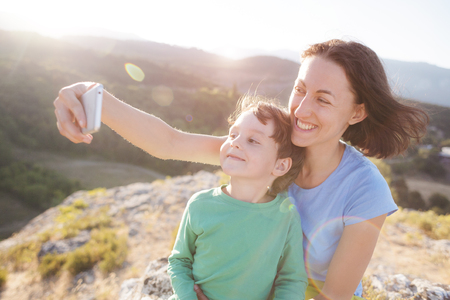 A woman with a boy on top of a mountain. Mom and her son make selfie on the background of a beautiful landscape. Traveling with a child.の写真素材
