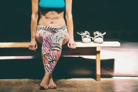 The climber rest after a workout. Training in the bouldering hall. A woman with a good press sits on a bench. A girl in a sports bra and tights. Naked belly. Climbing shoes.の写真素材