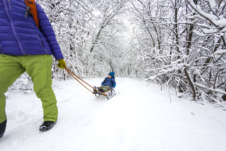 A woman is carrying a child on a sled. Mom walks with her son on the snow trail. Cheerful winter vacation. Winter fun. Baby on the sleigh.の写真素材
