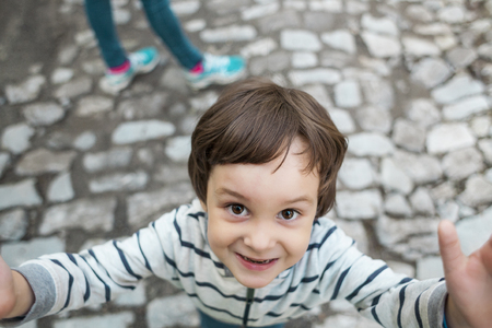 The child looks up. Portrait of a little boy. The kid walks along the city street. Cute little boy is smiling.の写真素材