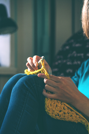 Girl knits crochet at home. Woman engaged in needlework. A knitter sits on a sofa and works. Creative hobby. Training patience and perseverance. Crochet thick yarn.の写真素材