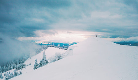 Silhouette of a man in the distance in the mountains. Winter landscape. Snow-covered mountains. A lonely man on top of a mountain. Dawn meeting.の写真素材