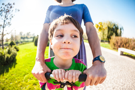 Woman riding with her son on a scooter. A boy with his mother riding in the park on a scooter. Happy holidays with parents. The girl in a dress and sneakers walks with the child.の写真素材