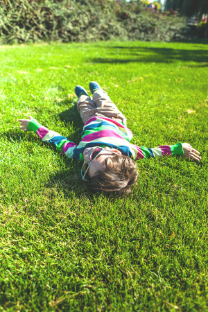 The boy is lying on the grass. The child is resting on a green lawn top view. Kid having fun on the lawn.の写真素材