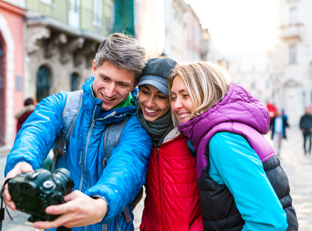 Friends take a selfie. Three friends are walking through the beautiful old town. Travel to European cities. Two women and a man are photographed against the backdrop of old buildings.の写真素材