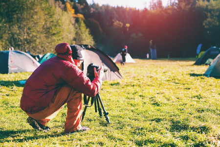 A photographer takes pictures of nature. Camera on a tripod. A man photographs beautiful views. Camping in the mountains.の写真素材