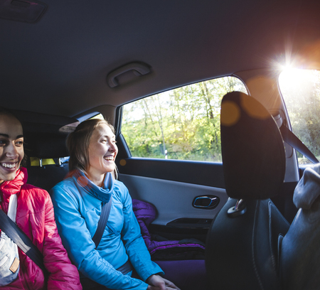 Two women in the back seat of a car. Girlfriends are hitchhiking. Passengers during a long trip. Travel by car.の写真素材