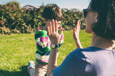 Mother plays with the child. A woman teaches her son to play with her palms. The boy is having fun with his mother on the grass. The kid gives five.の写真素材