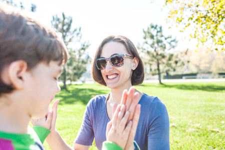 Mother plays with the child. A woman teaches her son to play with her palms. The boy is having fun with his mother on the grass. The kid gives five.の写真素材
