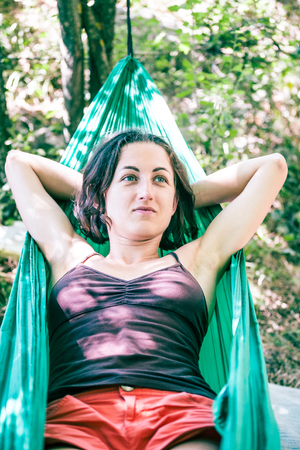 The girl is in a hammock. Woman resting lying in a green fabric hammock. Rest in the woods.の写真素材
