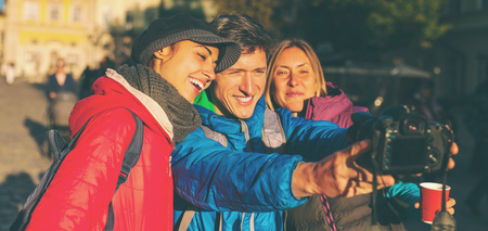 Friends take a selfie. Three friends are walking through the beautiful old town. Travel to European cities. Two women and a man are photographed against the backdrop of old buildings.の写真素材