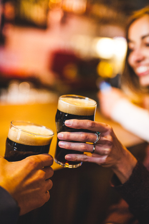 Woman and man drink beer. Friends met in a pub. Two glasses of dark beer. Couple on a date.の写真素材