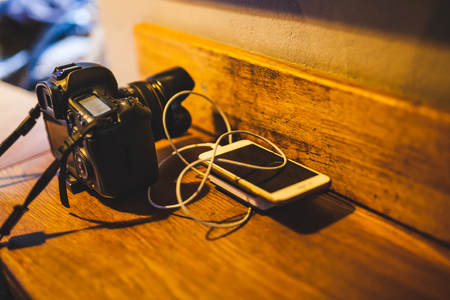 Camera, phone and powerbank on a wooden table. The smartphone is charging.の写真素材