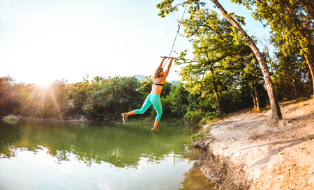 Jump into the water. A woman is resting on the lake. A swing from a rope and a stick. Active recreation in nature. Summer fun. A woman is riding a swing. Fisheye lens.の写真素材
