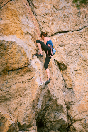 The girl climbs the rock. The climber is training to climb the rock. A strong athlete overcomes a difficult climbing route. Extreme hobby. A woman goes in for sports in nature. Natural rocky terrain.の写真素材