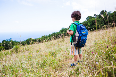 Child with a backpack in the forest. The boy walks along the mountain path. Active vacations. Traveling with children. The kid is studying nature.の写真素材