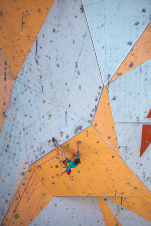 The climber trains on an artificial relief. A woman climbs a climbing route on a street climbing wall. Training in the hall. Strong girl involved in sports.の写真素材