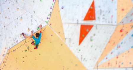 Training at the city climbing gym. A strong woman climbs a climbing route on artificial terrain. Slim girl involved in sports.の写真素材