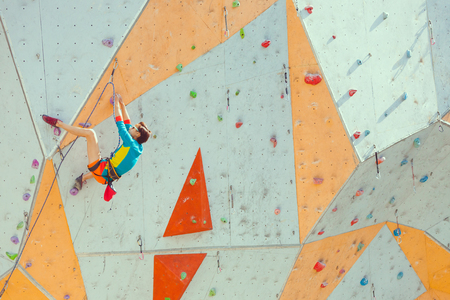 Training at the city climbing gym. A strong woman climbs a climbing route on artificial terrain. Slim girl involved in sports.の写真素材