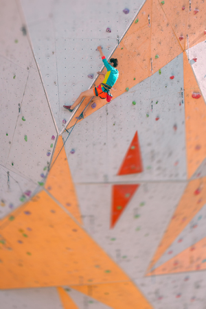 The climber trains on an artificial relief. A woman climbs a climbing route on a street climbing wall. Training in the hall. Strong girl involved in sports.の写真素材