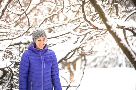 Portrait of a woman in a knitted hat. Smiling girl walks through the winter forest. Brunette on the...