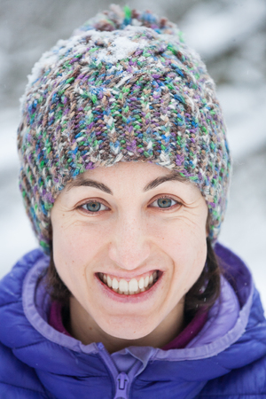 Portrait of a woman in a knitted hat. Smiling girl walks through the winter forest. Brunette on the background of snowy trees.の写真素材
