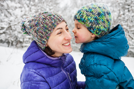 The kid hugs Mom. A boy with his mother on a winter walk. A child in a knitted hat kisses his mother. The woman supports her son. Motherhood. The family spends time together. Family values.の写真素材