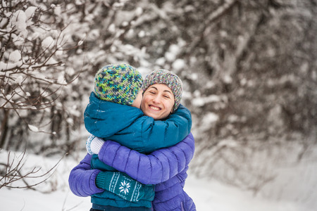 The kid hugs Mom. A boy with his mother on a winter walk. A child in a knitted hat kisses his mother. The woman supports her son. Motherhood. The family spends time together. Family values.の写真素材